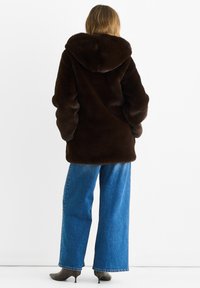 Brown faux fur hooded coat with a loose fit, long sleeves, and soft texture. Paired with wide-leg blue denim jeans and heeled boots.