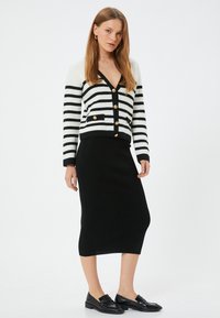 Gestreifter Cardigan in Schwarz und Weiß mit goldenen Knöpfen, kombiniert mit einem schwarzen gerippten Midirock und schwarzen Loafers. Schlichtes und tailliertes Design.