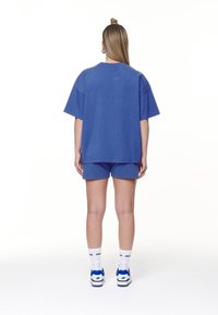 Blaues Baumwoll-oversized T-Shirt und passende Shorts. Das Outfit hat eine lockere Passform und wird mit weißen und blauen Turnschuhen sowie Socken kombiniert.