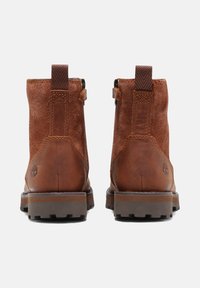Botas de tobillo de cuero marrón y ante con suela resistente, cierre por cremallera y un lazo en la parte posterior para ponerlas fácilmente. Logotipo de Timberland destacado.