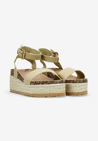 Sandalias de plataforma verde claro con tiras cruzadas, herrajes dorados y suela de yute texturizada. Suela de goma para tracción.