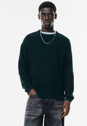 Grøn ribbet sweater med lange ærmer, rund halsudskæring, grå jeans og en sølvkæde. Glat tekstur, afslappet pasform og afslappet stil.