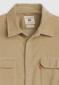 Tan corduroy shirt met een relaxte pasvorm, voorzien van een klassieke kraag, twee voren pockets en een klein rood Levi's label aan de zijkant.