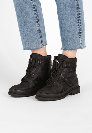 Bottes noires à lacets avec col rembourré et brides de marque, portées avec un jean bleu clair à ourlet effiloché.