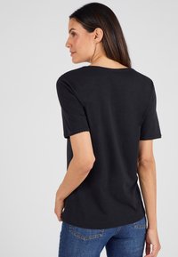 Top nero a maniche corte con colletto rotondo, dettagli a ondina sulle maniche, tessuto morbido e vestibilità rilassata, abbinato a jeans blu.