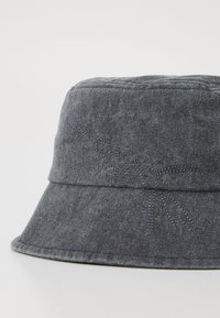 Gorra de cubo de algodón gris con una textura suave, que presenta un diseño cosido en la banda. Ala ancha y corona sin costuras para una comodidad óptima al llevarla.