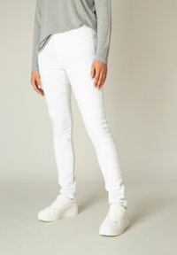 Witte spijkerbroek met een skinny fit en een gladde textuur, met een middelhoge taille. Gecombineerd met witte platform sneakers.