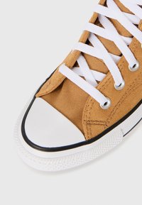 Barna vászon sneaker fehér fűzőkkel, gumis orr részes és fekete díszítéssel. Jellemzője a textúrázott felsőrész és a kontrasztos talpminta.