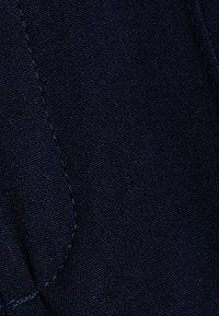 Donker denim stof met een gestructureerd oppervlak, voorzien van zichtbare stiksels en een licht vervaagd effect. Geen duidelijke patronen of hardwaredetails.