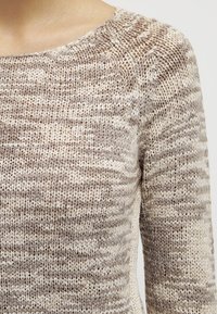 Maglione lavorato a maglia con scollatura rotonda. Presenta una combinazione di colori crema e marrone chiaro, con un motivo testurizzato e una trama larga.