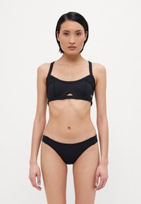 Črn bikini komplet, ki vključuje oprijet zgornji del s sprednjim izrezom in nastavljivimi naramnicami, v kombinaciji z nizkimi hlačkami, izdelanimi iz gladkega materiala.