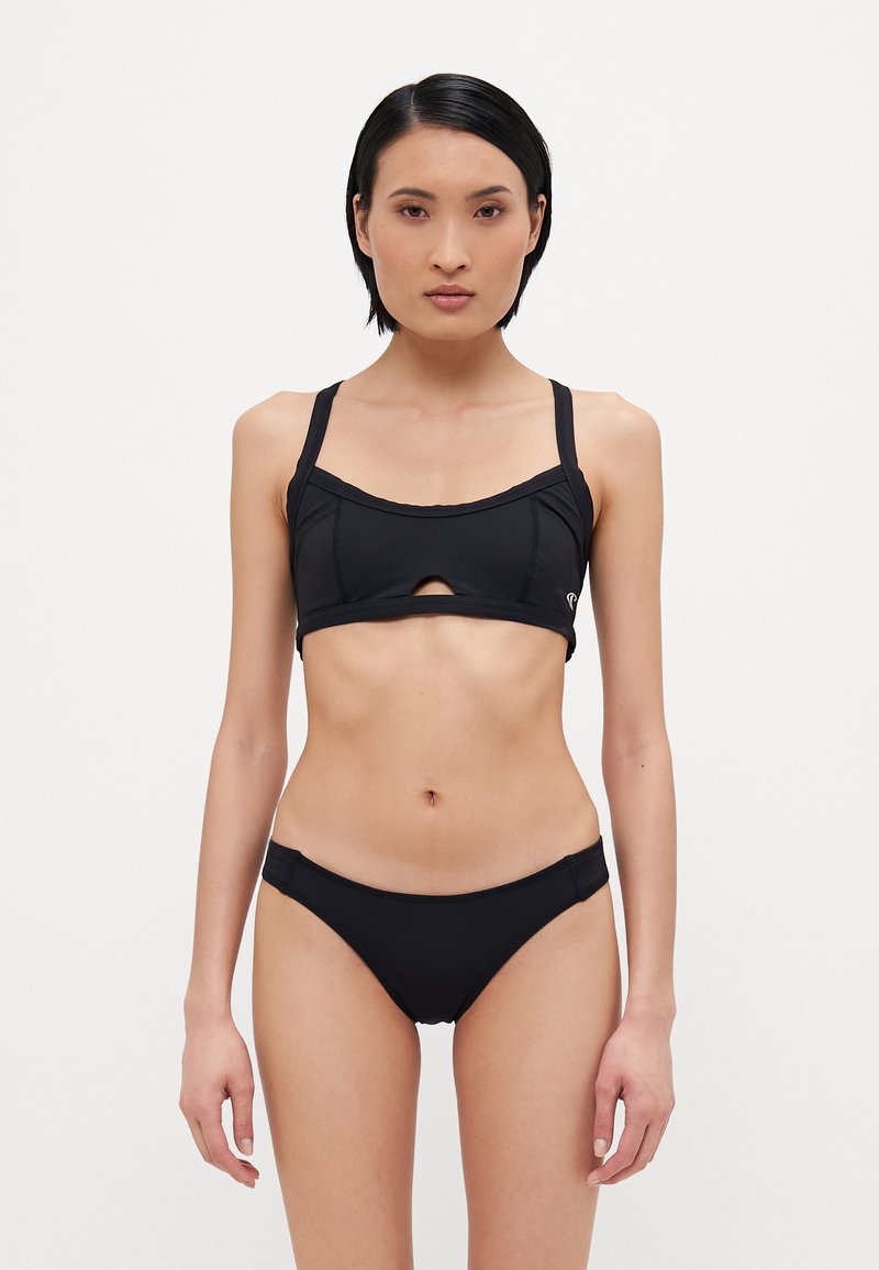 Črn bikini komplet, ki vključuje oprijet zgornji del s sprednjim izrezom in nastavljivimi naramnicami, v kombinaciji z nizkimi hlačkami, izdelanimi iz gladkega materiala.