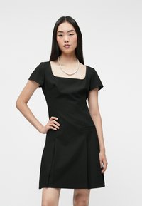 Μαύρο φόρεμα με κοντό μανίκι και τετράγωνη λαιμόκοψη, εφαρμοστό μπούστο, διακριτικές πλαϊνές τσέπες και φουσκωτό φουστάνι. Λείο ύφασμα με κλασικό σχέδιο.