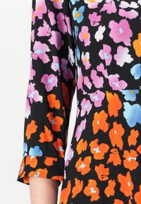 Črna tkanina z živahnim cvetlično vzorcem v roza, oranžni in modri barvi. Rokav do tri četrtine z možnostjo zavihanja. Gladka tekstura.