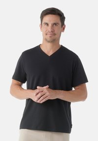 Black short-sleeve V-neck t-shirt made of soft fabric, featuring a relaxed fit and plain design, worn by a man with hands clasped.