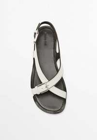 Black leather sandal with white cross-strap, adjustable buckle. Open heel design with smooth texture and subtle stitching detail.