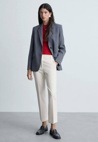 Blazer gri cu dungi, pulover tricotat roșu, pantaloni crem tailorați și loafers negri. Material neted și siluetă structurată.
