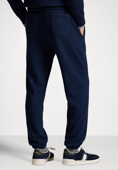 Joggers azuis marinho canelados apresentam um bolso traseiro e punhos afunilados. Combinados com ténis escuros e meias cinzentas com padrão.