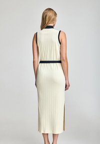 Vestido sin mangas de color crema con un corte ajustado, detalles de acento en negro y una abertura lateral en el dobladillo.