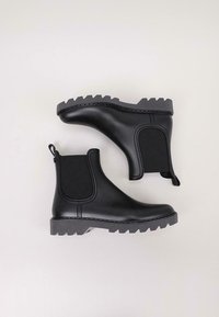 Botas de tobillo negras de goma suave con paneles laterales elásticos, suelas de goma texturizada y un tirador en el talón para facilitarlas al ponerlas.