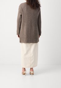 Lång, ribbad cardigan i taupeull, med lång ärm, sidoflikar och en avslappnad passform, kombinerad med en beige maxikjol och remsandaler.