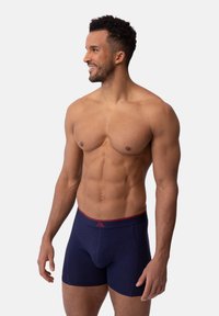 Navy boxer briefs with a red waistband, cotton blend material, fitted design, and a slight sheen, highlighting contours and seams.