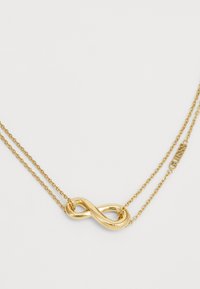 Collier en or à double couche avec un pendentif en forme d'infini, texture lisse et une petite étiquette gravée "GUESS".