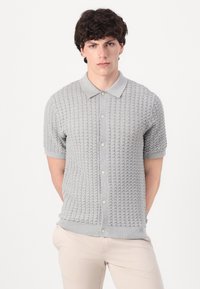 Tricou polo tricotat de culoare gri deschis, cu mâneci scurte, având un model texturat, închidere cu nasturi și guler și manșete în contrast.