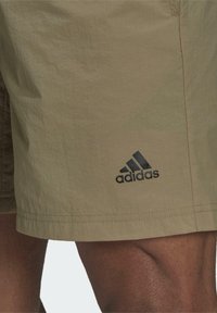 Beiga shorts i lättviktsmaterial, med en svart Adidas-logotyp på nedre vänstra benet, med sicksackad nederkant och strukturerad yta.