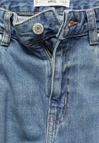 Vaqueros de mezclilla de color azul claro y desgastado. Cuentan con un botón de metal, cierre de cremallera y costuras naranjas. Textura suave y diseño clásico de cinco bolsillos.