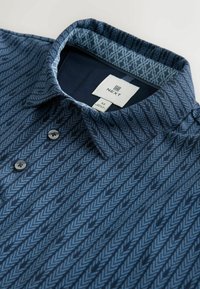 Camisa de cuello con estampado azul con botones, con un forro interior del cuello azul oscuro y etiqueta visible de la marca "NEXT" talla M.