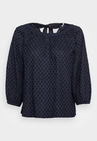 Blusa blu navy con maniche a sbuffo, scollatura raccolta e chiusura con fiocco sul retro. Il tessuto trasparente presenta ricami floreali in tutto il capo.