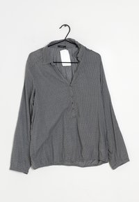 Langärmlige Bluse aus grauem Stoff mit einem dezenten geometrischen Muster, ausgestattet mit einem Kragen und einer Knopfleiste, die an einem schwarzen Haken hängt.
