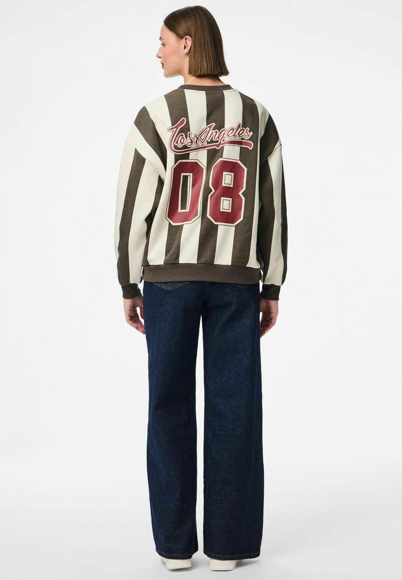 Il pullover presenta strisce marroni e crema, una grafica "Los Angeles", un grande "08" bordeaux e polsini elasticizzati, abbinato a jeans a gamba larga.