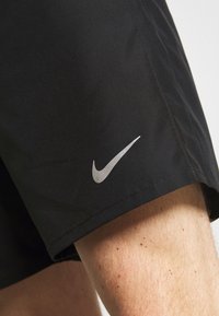 Schwarze Sportshorts aus leichtem Material. Mit einem silbernen Nike-Logo am Saum. Glatte Textur mit klaren Nähdetails.