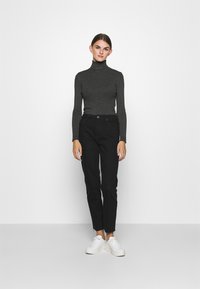 Sivi rebrasti rolak, uparen s uskim crnim trapericama. Model nosi bijele platforme. Jednostavan, elegantan dizajn bez vidljivih uzoraka.