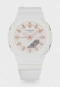 Valge G-Shock kell ümmarguse näo, roosakuldsete aktsentidega, digitaalse ekraaniga ja silikoonrihmaga. Veekindel kuni 20 baari.