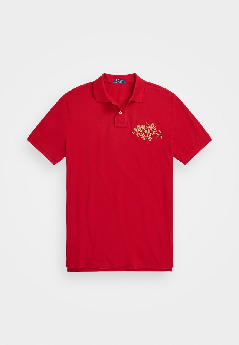 Polo rouge avec col et deux boutons, arborant un logo brodé en or de trois joueurs de polo à cheval sur la poitrine gauche.