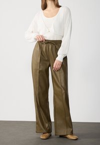 Vit stickad kort cardigan, långa ärmar, detalj med gyllene knappar; olivgröna läderbyxor med vida ben, dragsko och sidofickor.