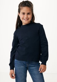 Marinblå ribbad stickad tröja med rund halsringning och långa ärmar; har åtsittande manschetter och nederkant. Bärs med blå denimjeans.