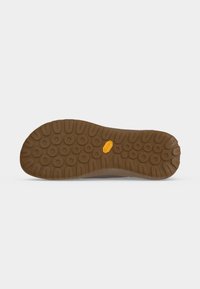 Semelle de chaussure marron avec motif circulaire, profondes rainures et un petit logo jaune Vibram au centre, présentée sur fond blanc.