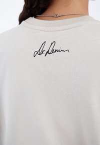 Světle šedá mikina vyrobená z bavlny, se žebrovaným výstřihem a logem "Dr. Denim" vyšitým černě na zadní straně.