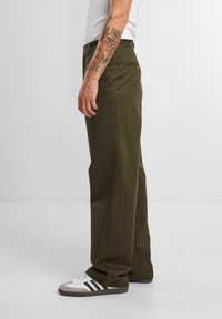 Olijfgroene katoenen broek met een recht pijpdesign, twee zijzakken en een soepele textuur. Gedragen met witte en grijze schoenen.