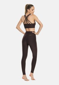 Rjav športni modrček z zareznimi naramnicami in visoko pasom ujemajoče se legice, ki poudarjajo gladko teksturo in subtilno oznako.