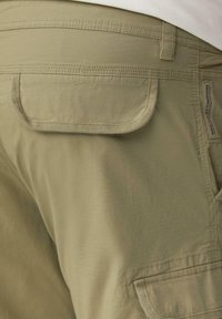 Close-up van kaki cargobroek met achterzak met flap en gestikte label aan de rechterkant.
