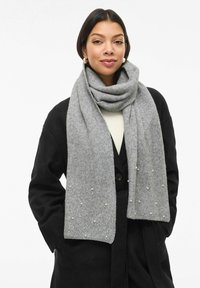 Sivi vuneni šal s mekanom teksturom, ukrašen ukrasnim perlastim detaljima i elegantnim nabiranim slojem, nošen preko crnog kaputa.