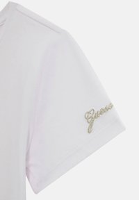 T-shirt bianco a maniche corte, con una finitura testurizzata sottile e il logo "Guess" ricamato in oro vicino al polsino.