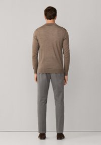 Bruine wollen trui met een ronde hals, lange mouwen en een aansluitend design, gecombineerd met lichtgrijze broeken en donkere schoenen.