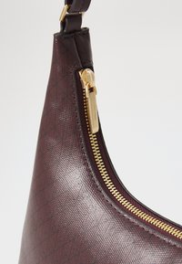 Geantă synthetic burgundy cu un finisaj texturat, având un fermoar de culoare aurie și accente cu un model diagonal pe suprafață.