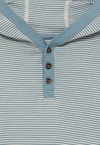 Gestreifter hellblauer Henley-Hemd mit weicher Textur, ausgestattet mit einem Rundhalsausschnitt, drei braunen Knöpfen und kontrastierenden weißen Streifen.